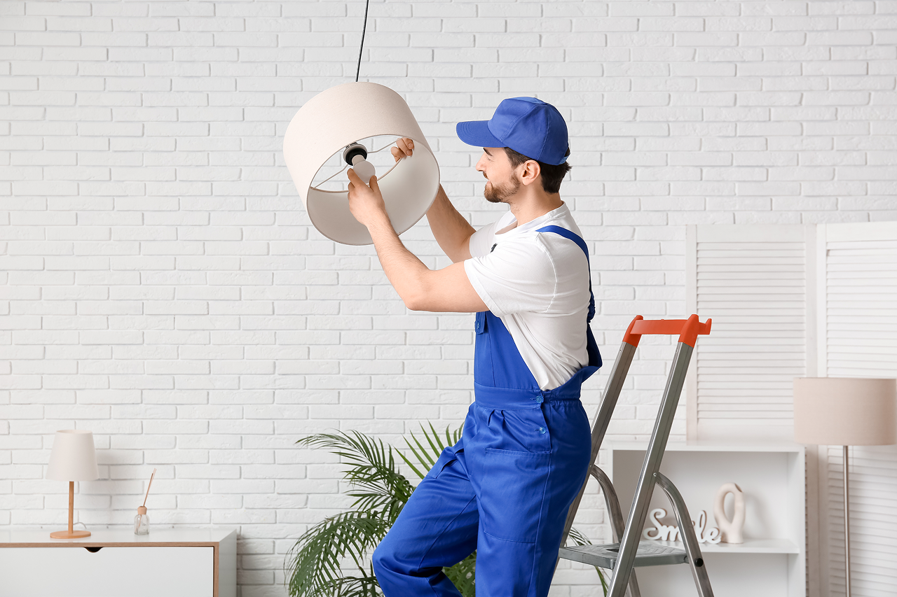electrician changing light bulb in hanging lamp at home